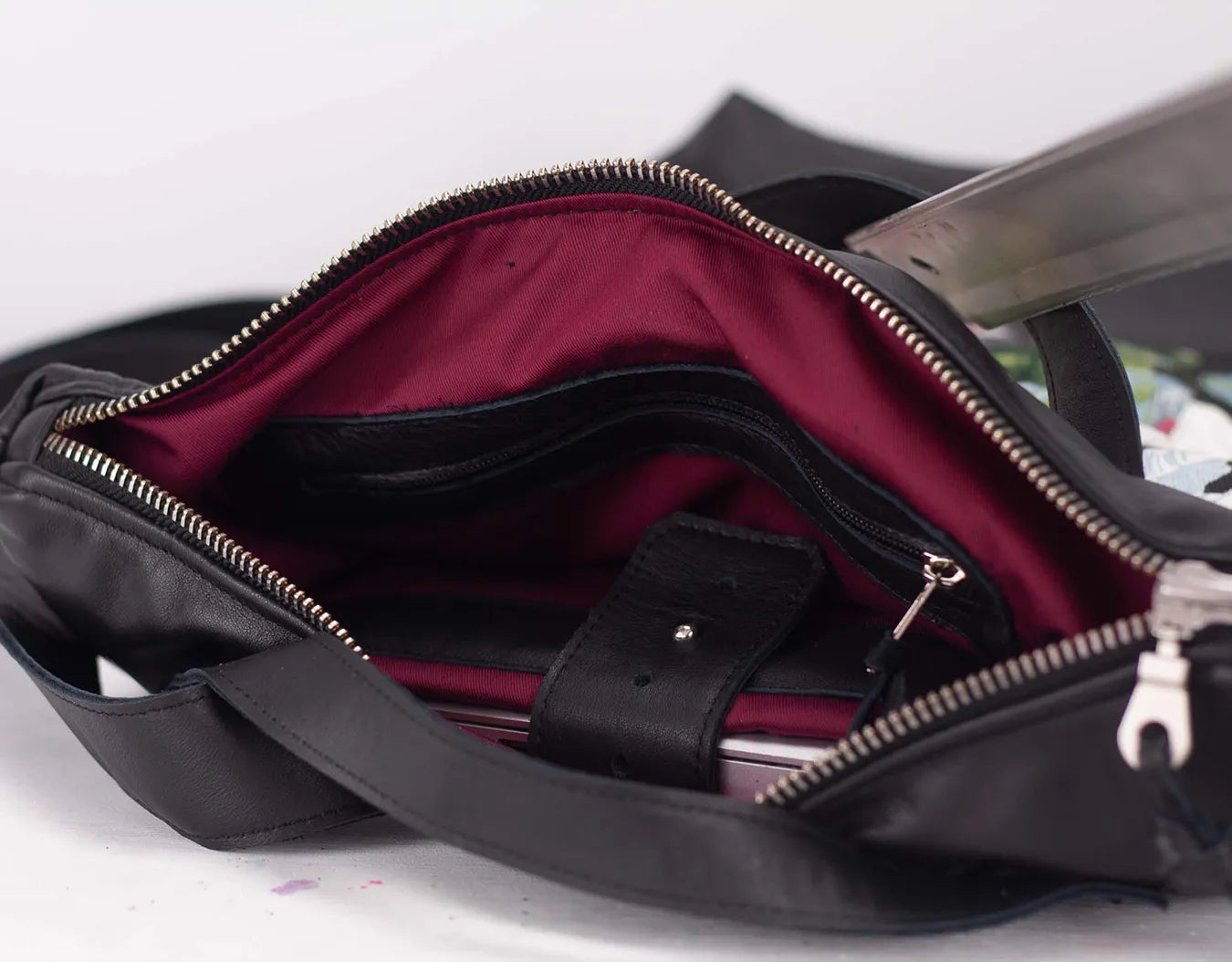 Black handbag with open zipper showing a red interior on a light gray background