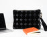 Black textured pouch next to a laptop and books on a white background