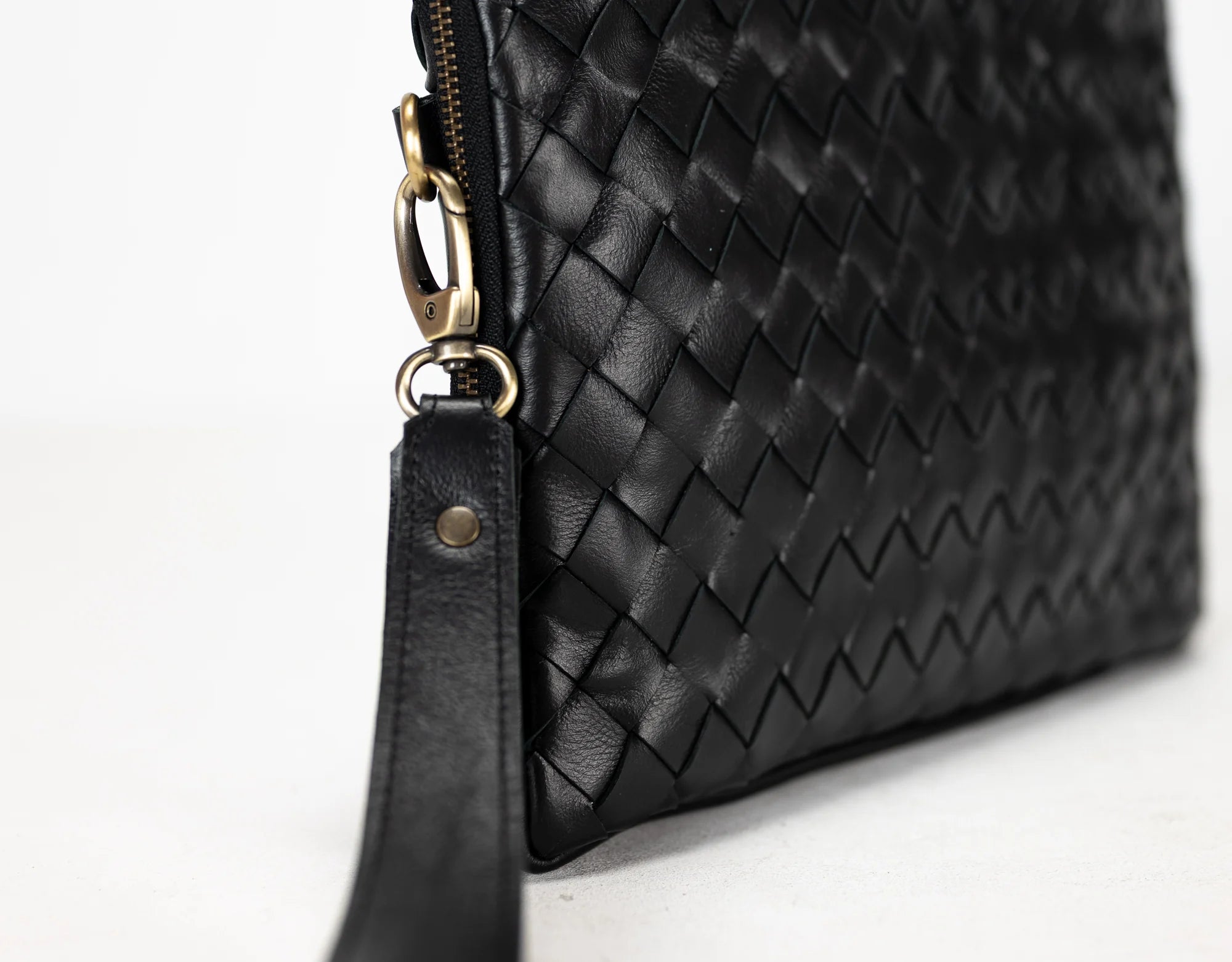 Black woven leather clutch bag with gold zipper on a white background