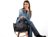 Woman sitting on a stool with a black leather handbag on a white background