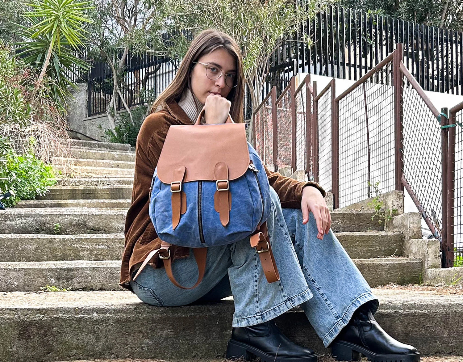 Person sitting on steps wearing a blue backpack with brown leather straps.