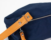 Navy blue bag with a tan leather strap and zipper on a white background