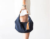 Navy blue handbag with a tassel held by a person on a white background