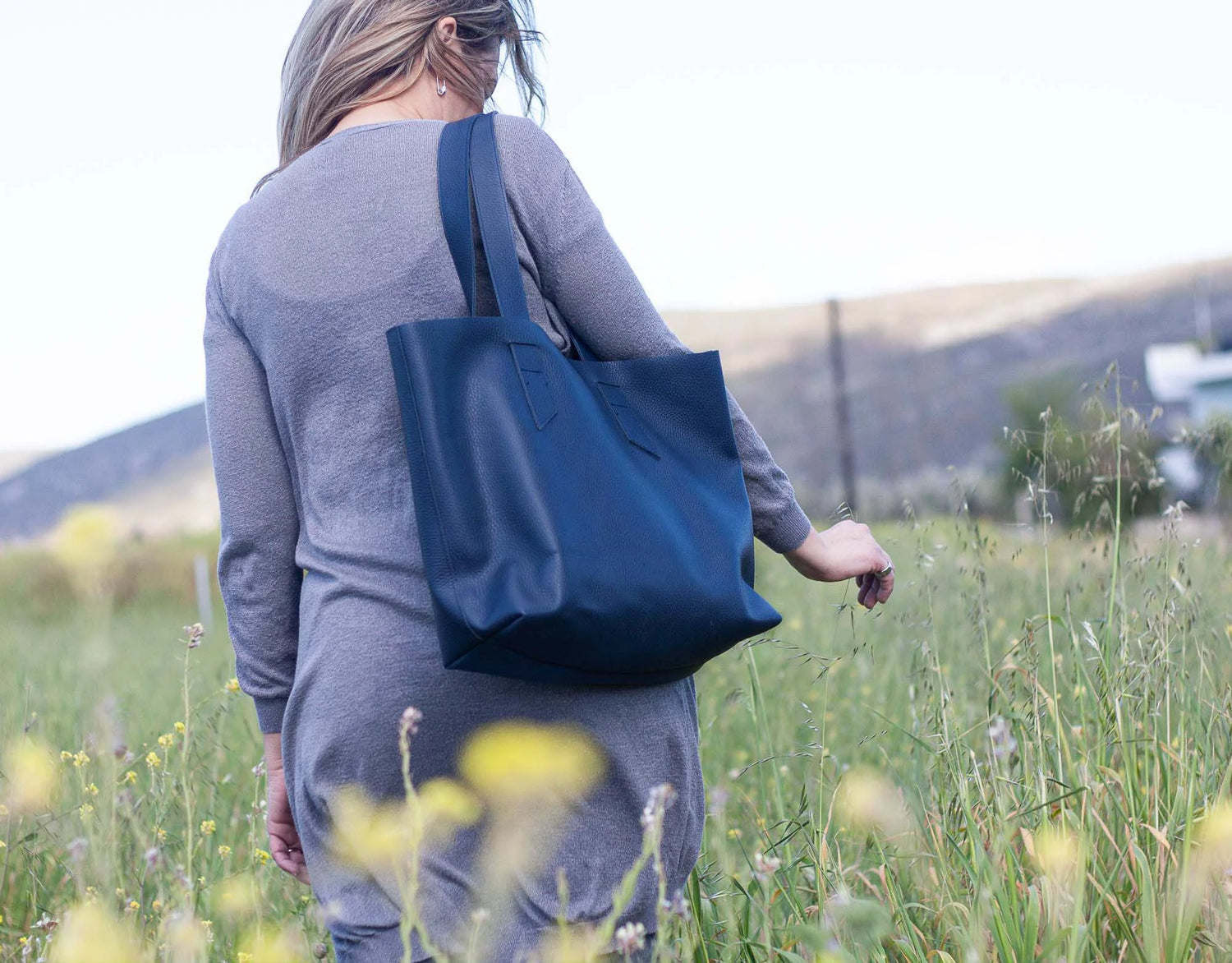 Person walking in a field with a blue tote bag