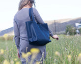 Person walking in a field with a blue tote bag