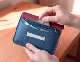 Blue leather wallet with a pink interior being held by a hand on a wooden surface.