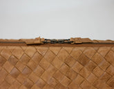 Close-up of a brown woven leather clutch bag with a zipper on a light gray background