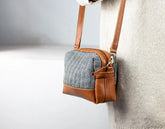 Handbag with brown leather strap and patterned body against a neutral background