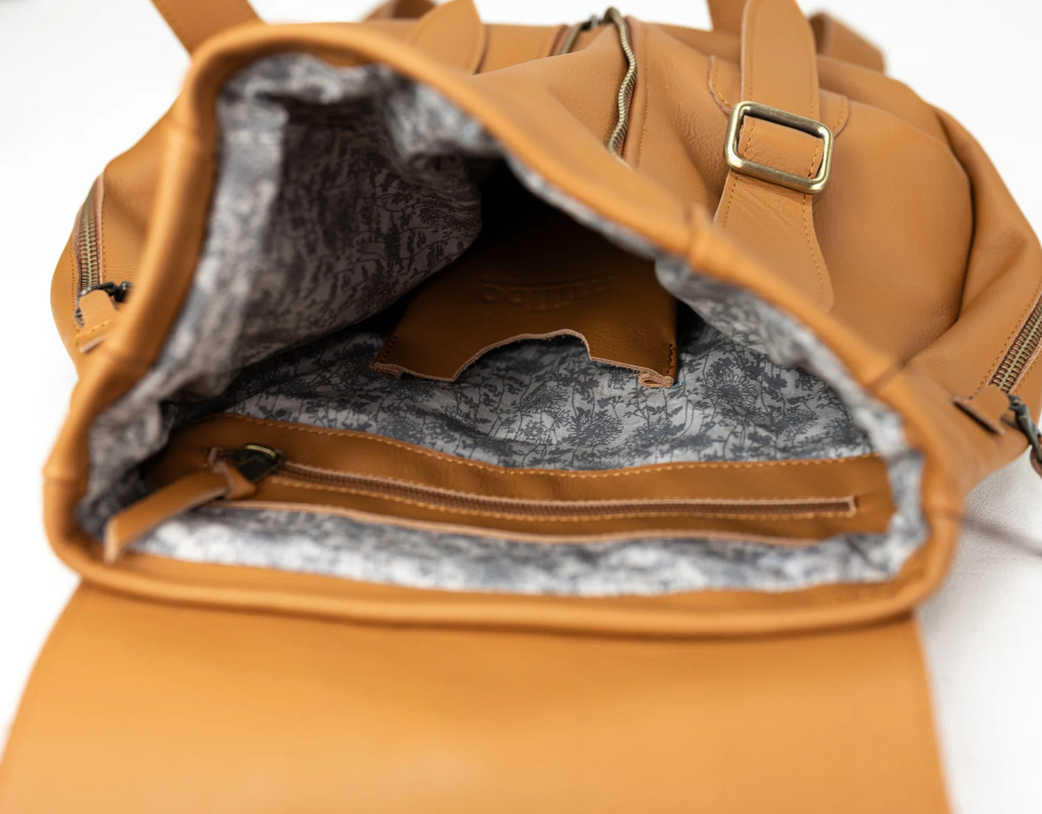Brown leather backpack with open front pocket showing gray interior.