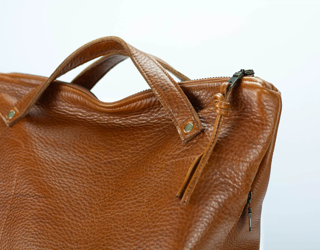 Brown leather handbag with a visible zipper on a light gray background