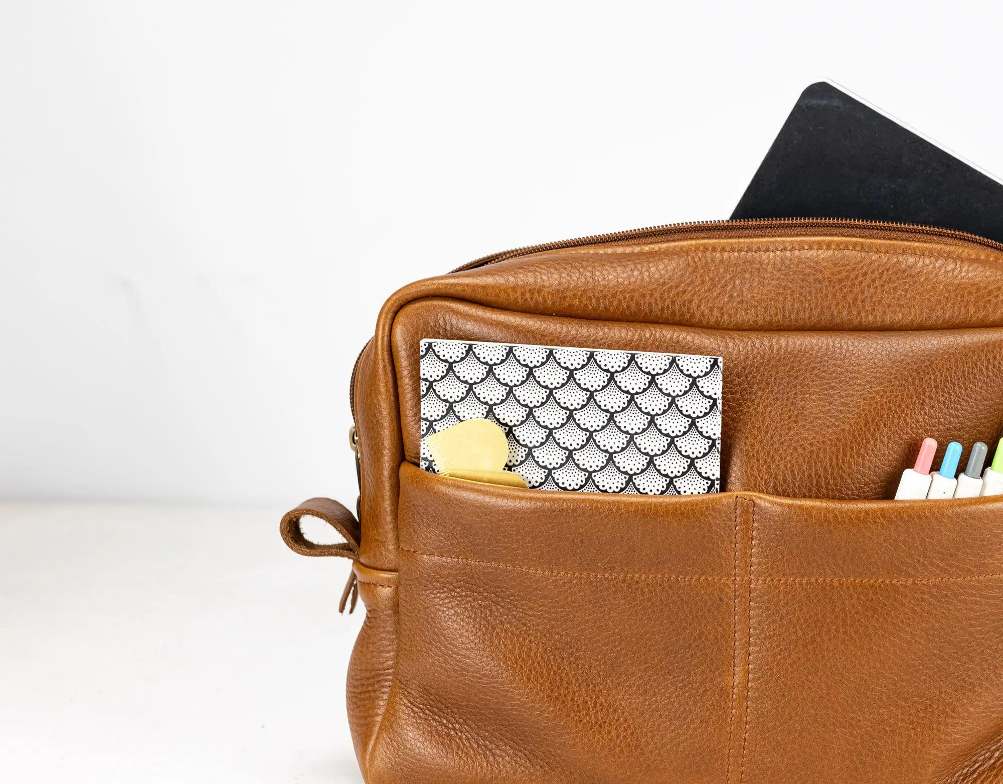 Brown leather bag with compartments containing stationery items on a white background