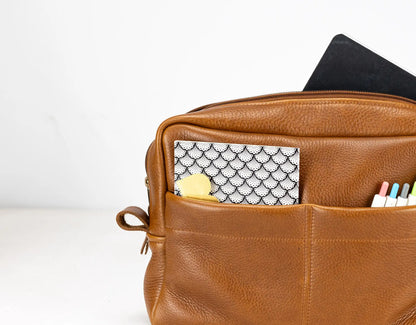Brown leather bag with compartments containing stationery items on a white background