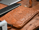 Brown leather clutch on a wooden surface with a keyboard in the background