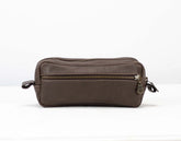 Brown leather toiletry bag with zippers on a white background