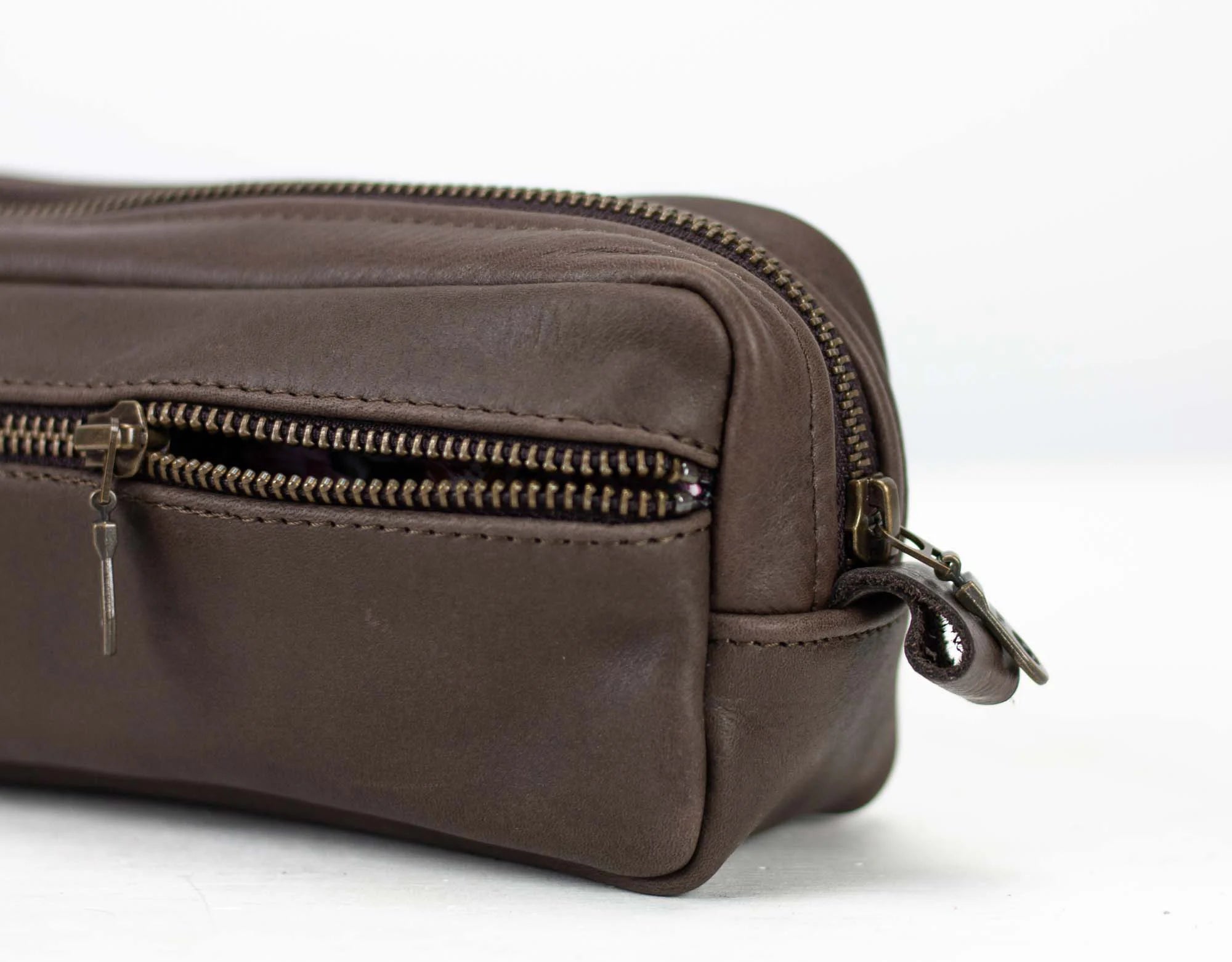 Brown leather toiletry bag with zippers on a white background