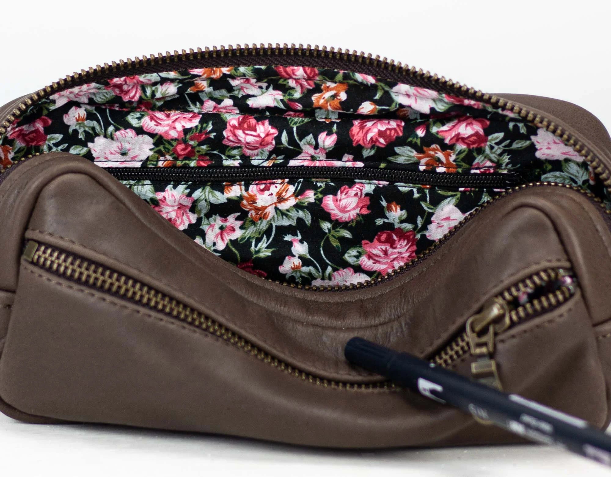 Brown leather bag with floral interior and pen on a white background