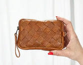 Brown woven clutch held by a hand against a white background