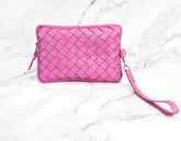 Pink woven clutch with a wrist strap on a white marble background