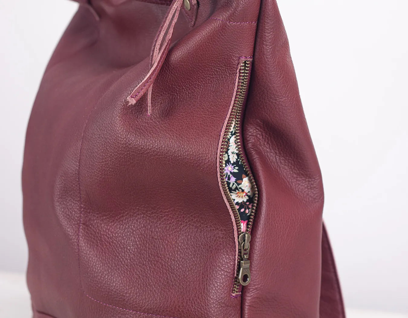 Close-up of a maroon leather bag with floral zipper pull on a white background
