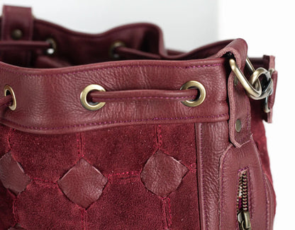Close-up of a maroon leather handbag with gold hardware on a white background