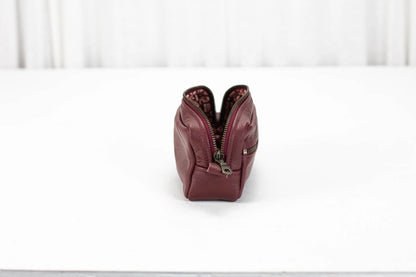 Maroon leather zippered pouch on a white surface with a white background