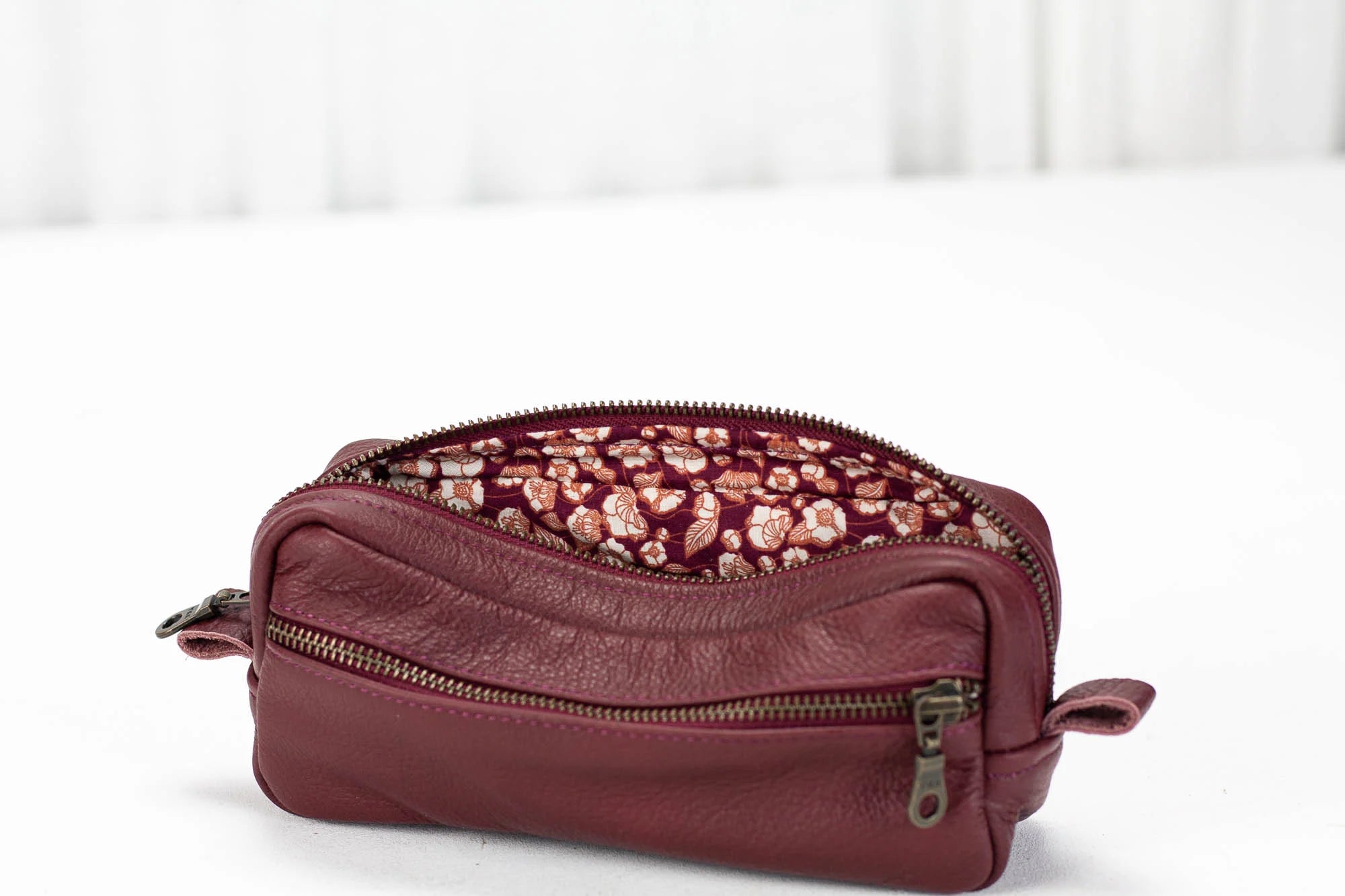 Maroon leather toiletry bag with floral patterned interior on a white background