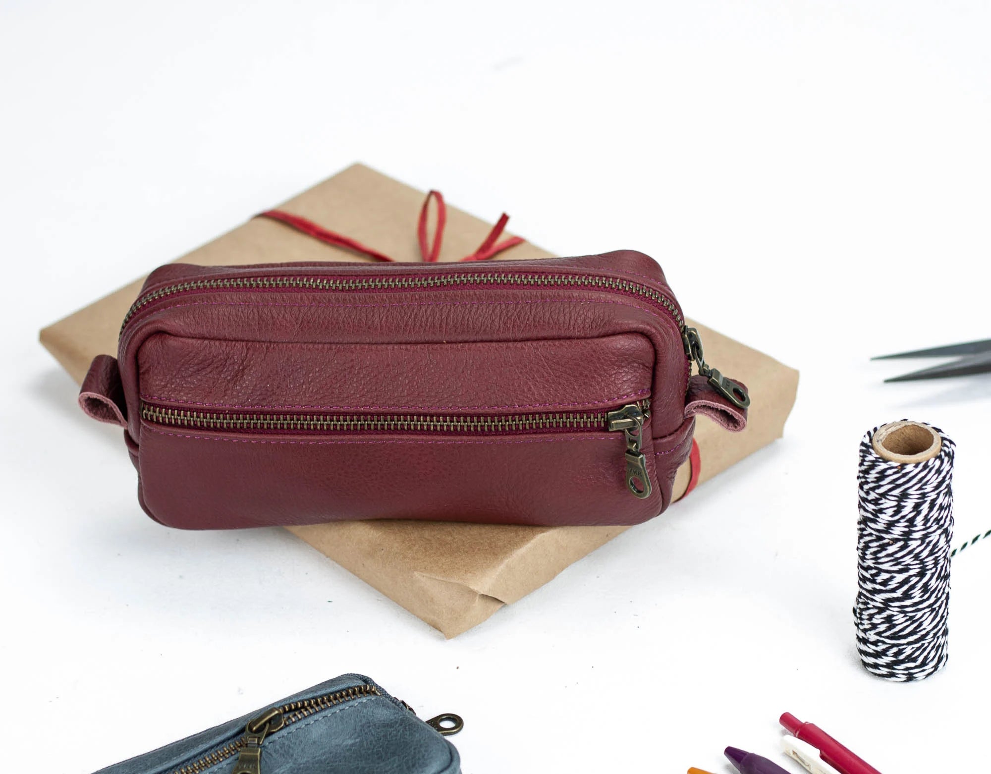 Maroon leather pencil case on a white background with stationery items.