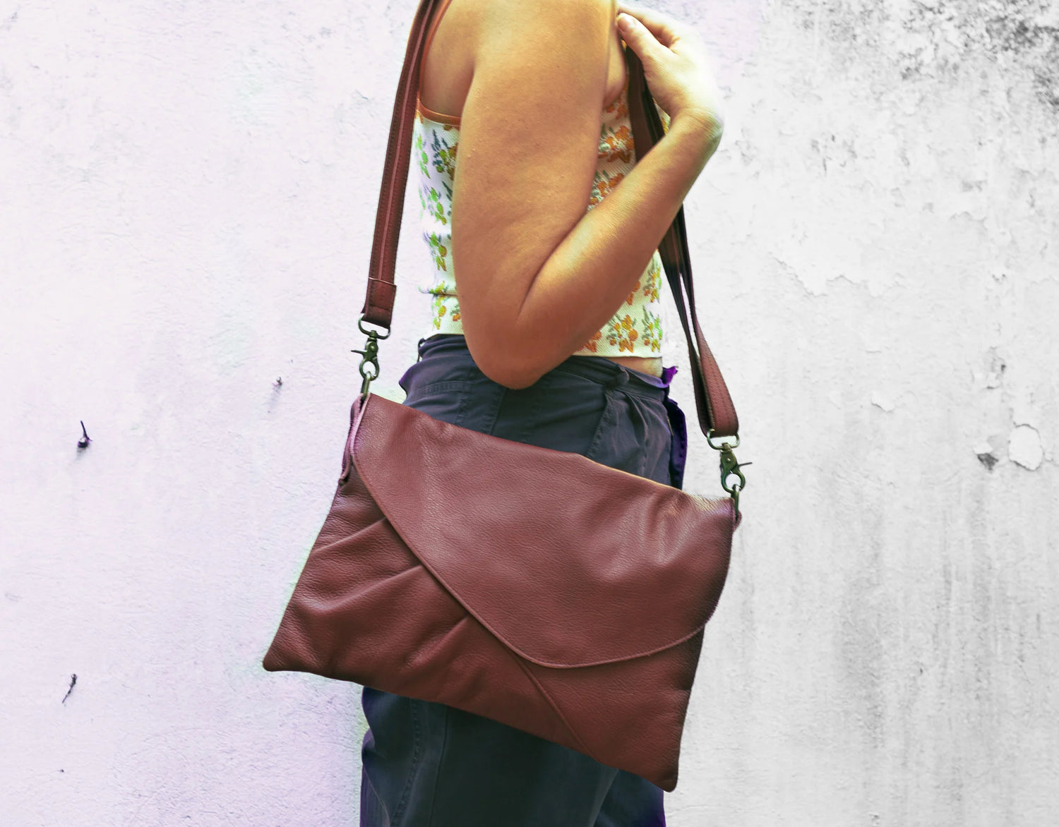 Person holding a brown leather bag against a textured white wall