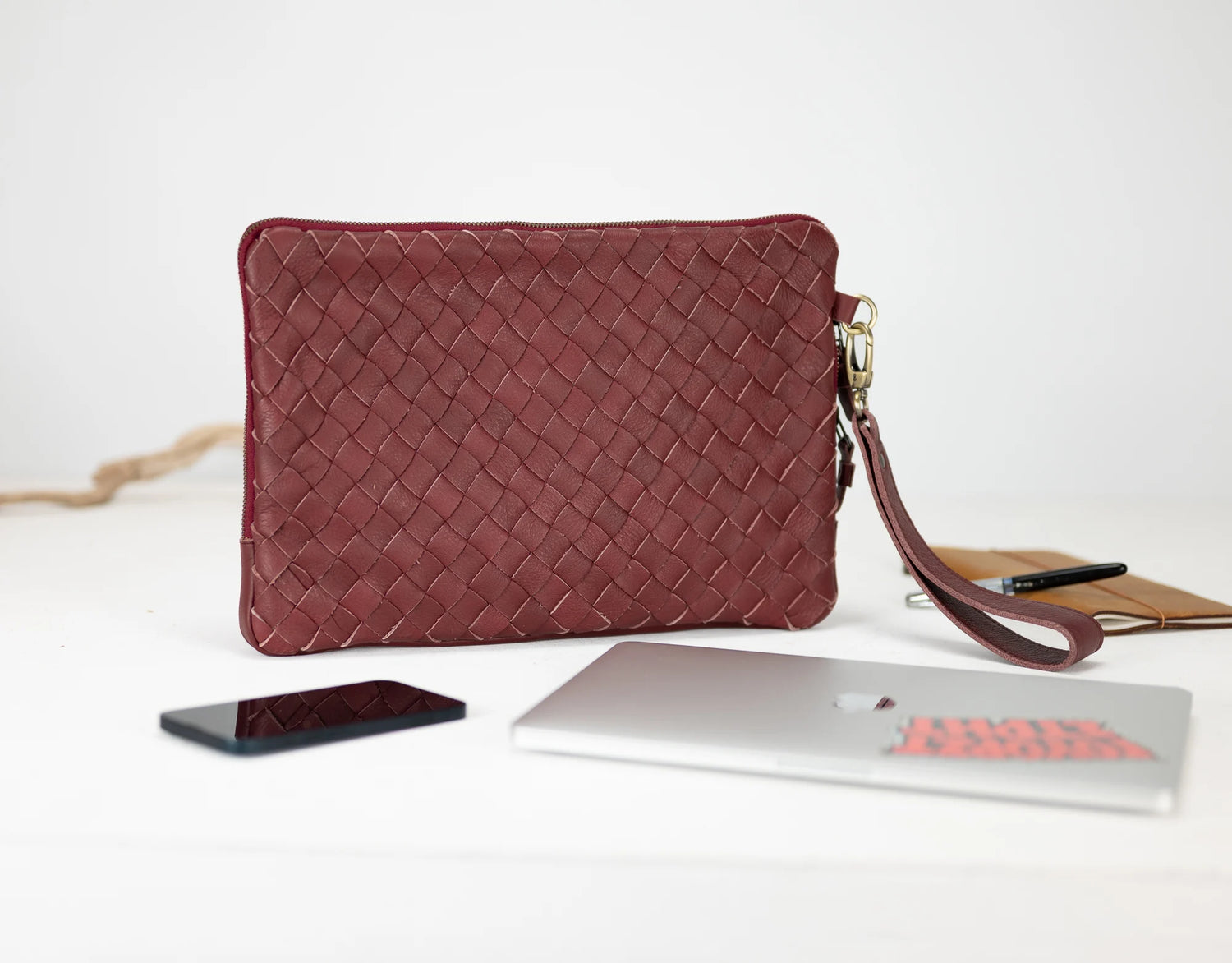 Red woven clutch bag on a white surface with a phone and laptop.