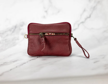 Red leather wristlet with a zipper on a marble surface