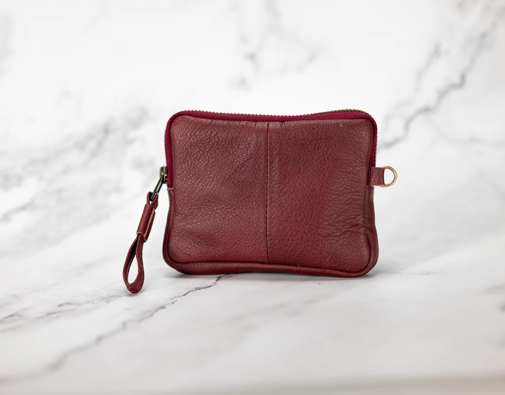 Red leather pouch with a strap on a marble background