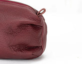 Close-up of a maroon leather pouch with a zipper on a white background