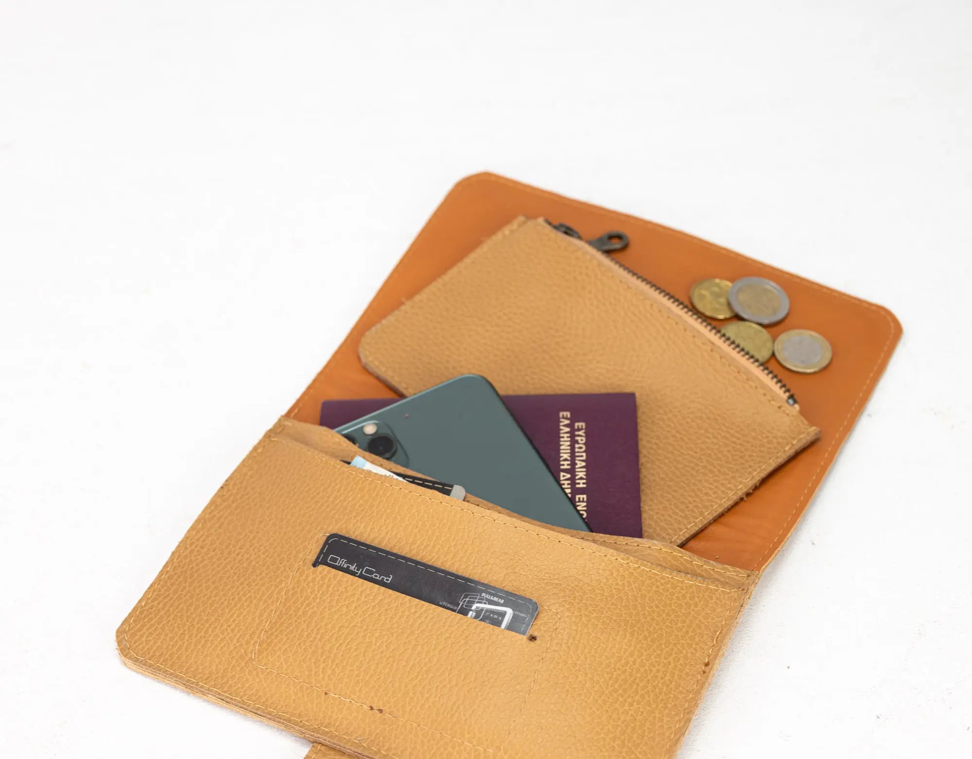 Open tan leather wallet with phone, passport, and coins on a white background