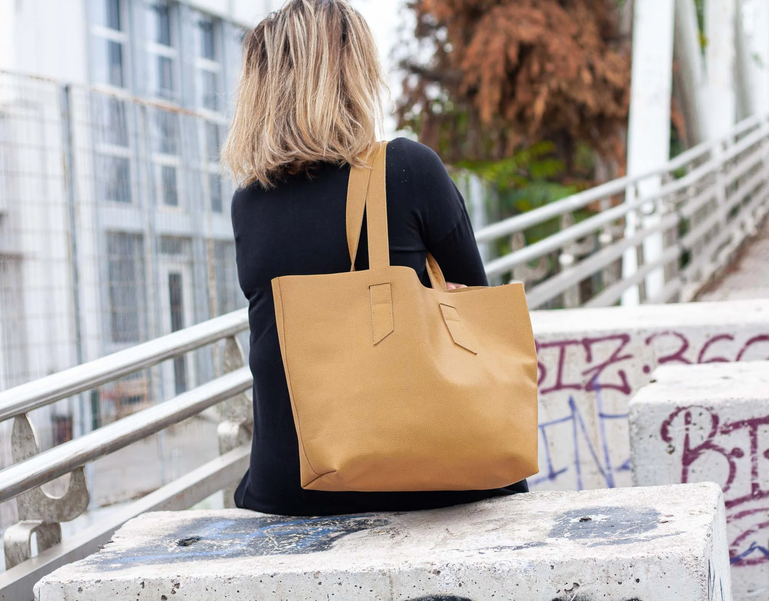 Person sitting on a bench with a caramel tote bag over their shoulder