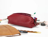 Red leather pencil case with stationery items on a white surface