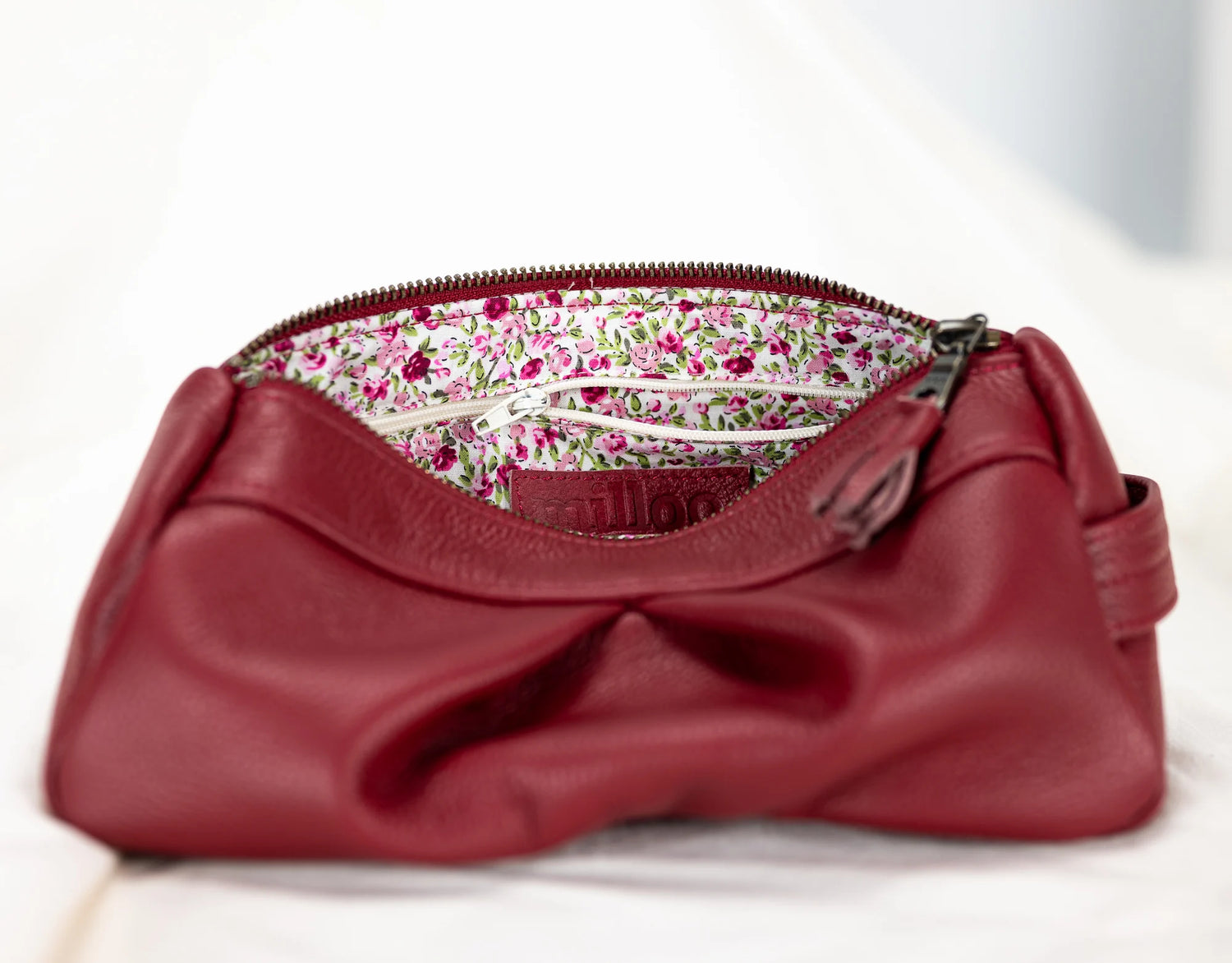 Red leather clutch bag with floral interior lining on a white background