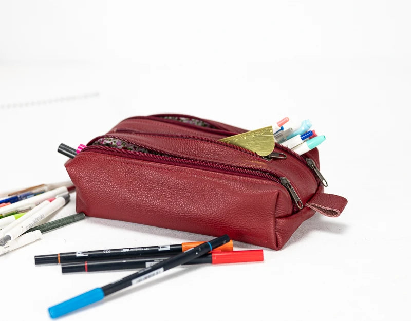 Red leather pencil case with stationery items on a white background#color_deep-red