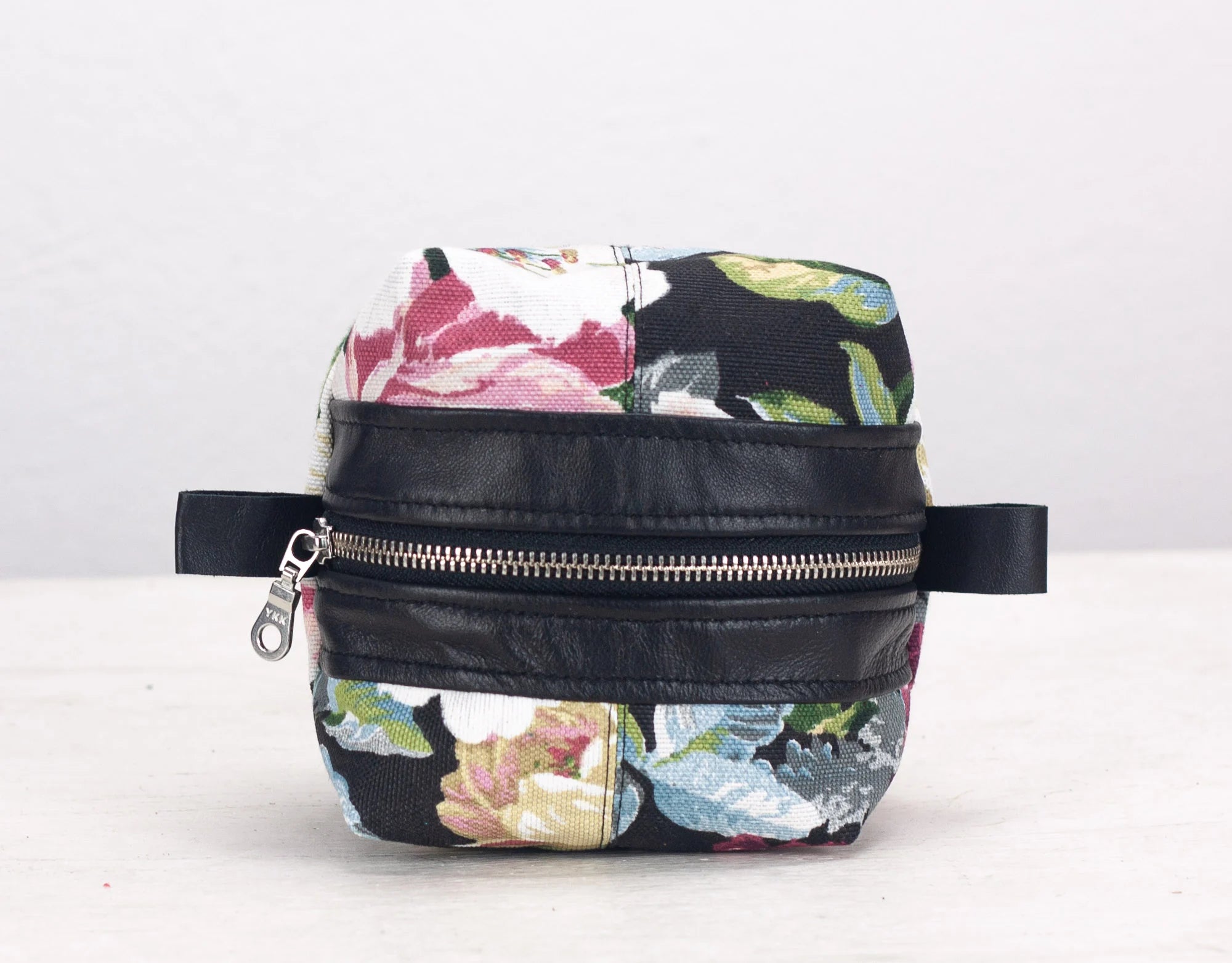 Floral-patterned bag with black leather accents on a white background