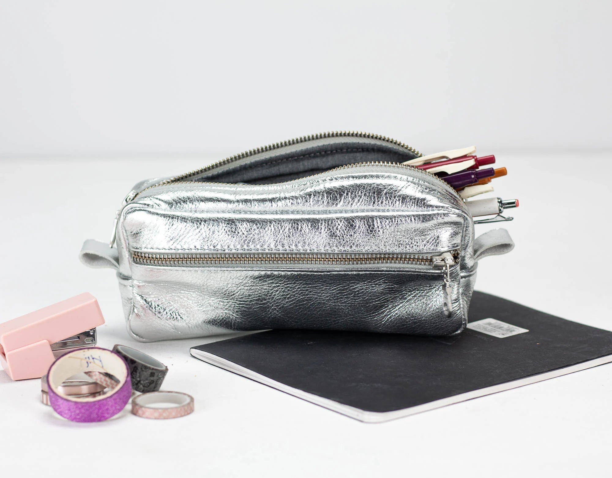 Silver pencil case with stationery items on a white background