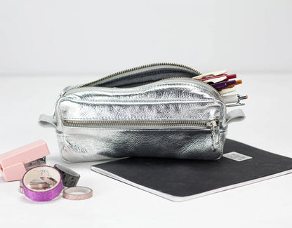 Silver pencil case with stationery items on a white background