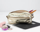 Gold metallic pencil case with stationery items on a white background