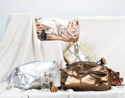 Gold and silver makeup bags with perfume bottles on a white surface