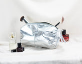 Silver cosmetic bag with makeup items on a white surface