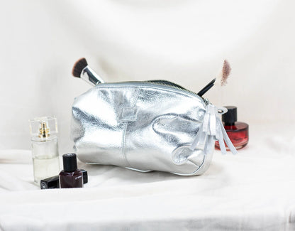 Silver cosmetic bag with makeup items on a white surface