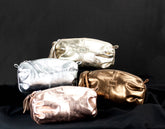 Four metallic pouches in silver, gold, and bronze on a black background