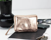 Rose gold pouch on a white surface with a plant and phone in the background