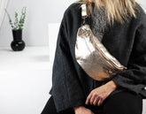 Person wearing a metallic silver fanny pack in a minimal indoor setting.