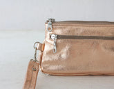 Rose gold clutch bag with a strap on a light wooden surface