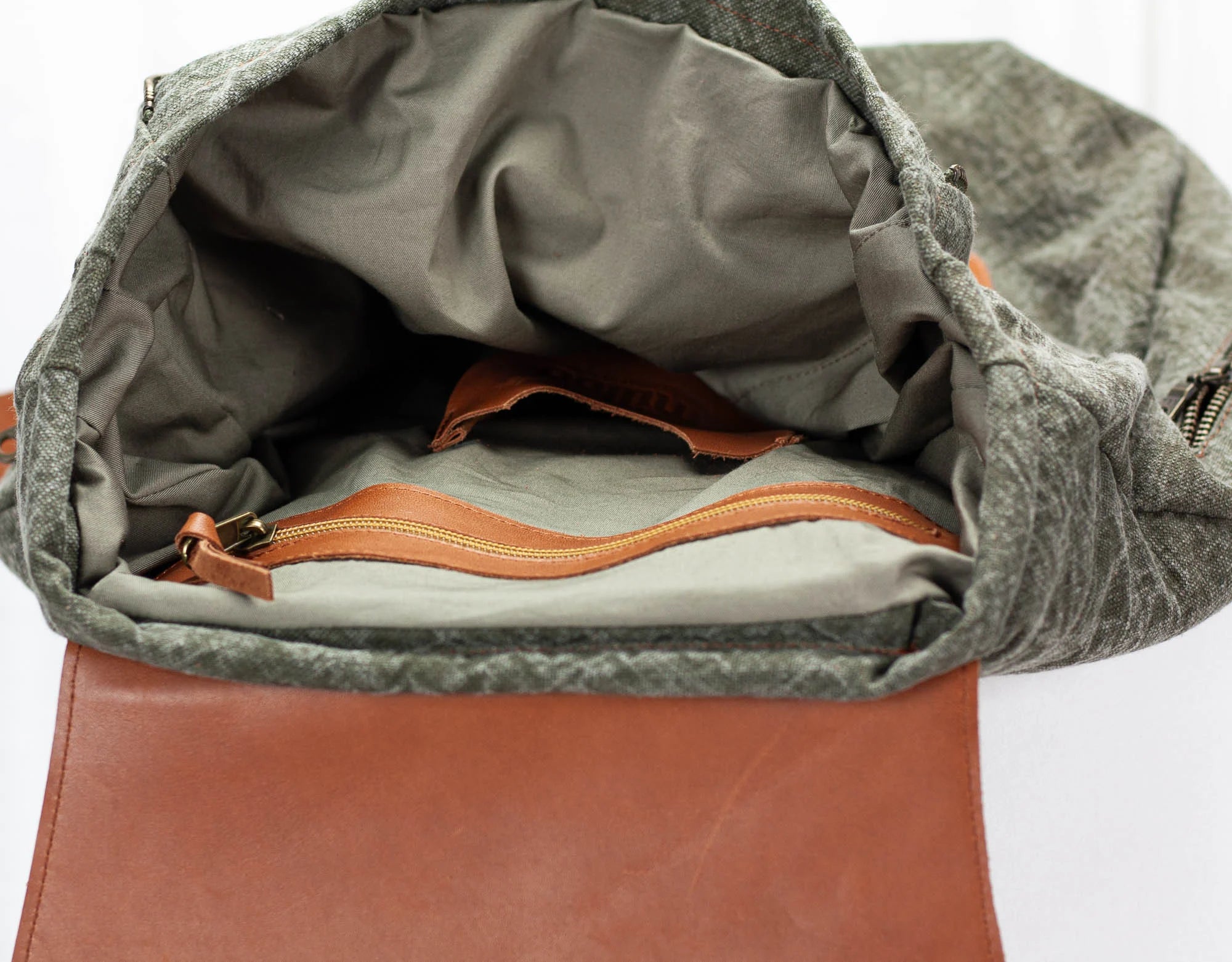Open green backpack with brown interior and zipper on a white background
