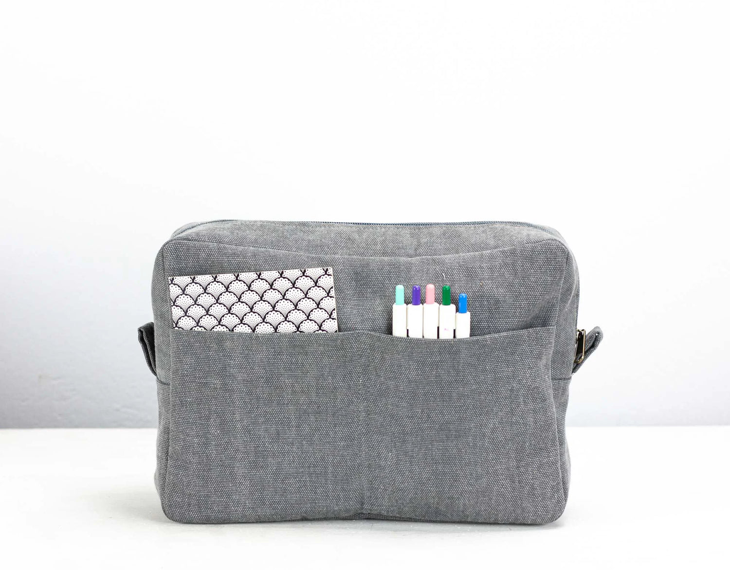 Gray fabric pouch with a pocket and markers on a white background